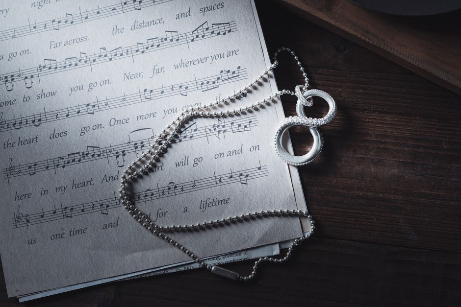 音楽の楽譜の上にある銀のネックレスのクローズアップで、タコの触手デザインが特徴的で、アーティスティックな雰囲気を醸し出しています。