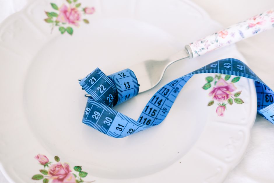 ダイエットや健康的な食事を象徴する、フォークと青いメジャーが付いた花柄の皿。