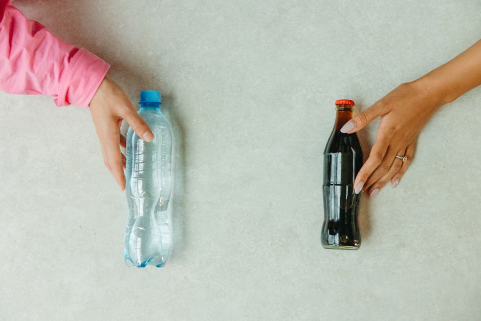 明るい表面の上で水のボトルとソーダのボトルに手が伸びるクローズアップ。