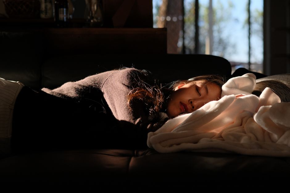 窓から差し込む温かい日差しの下でソファの上で穏やかに眠る女性。